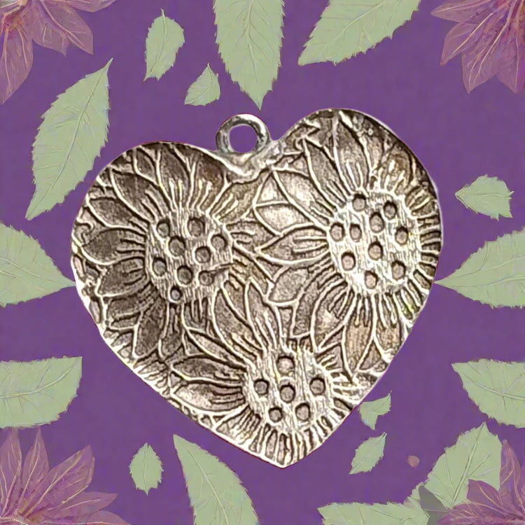 A heart shaped silver pendant made with silver clay, using a debossed texture mat. A large sunflower design. The customer has used the design to adorn the back of her pendant.