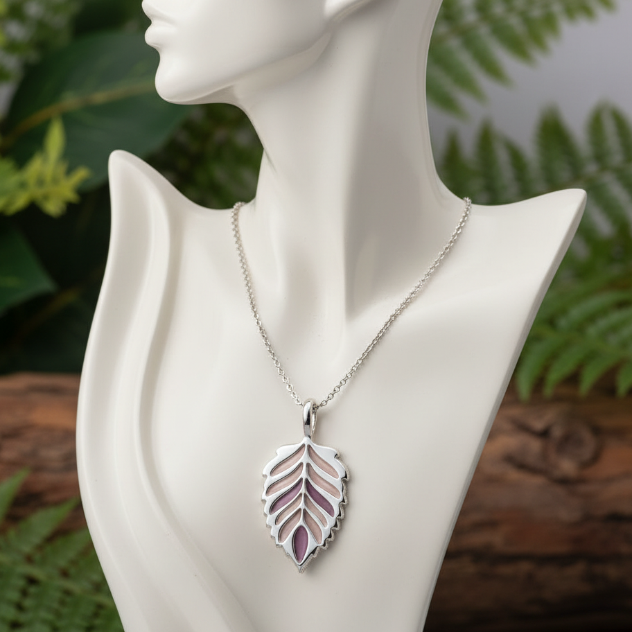 Silver necklace with a leaf-shaped pendant on a mannequin bust against a natural background.