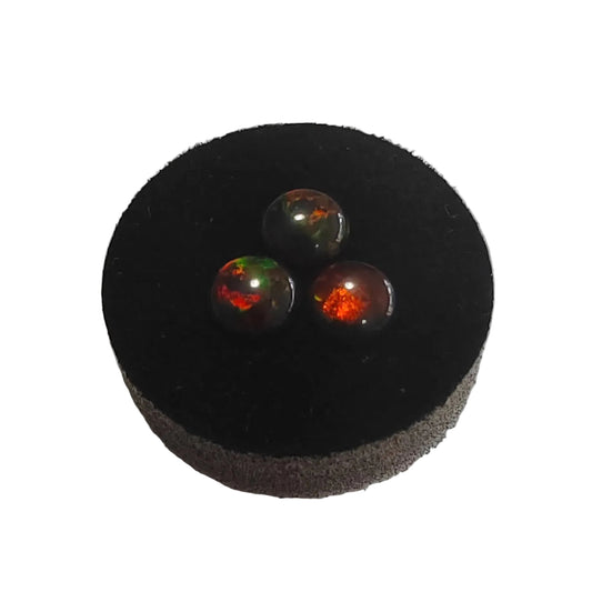 Three fireable Black opals cabochons with red fire on a black cushion against a white background