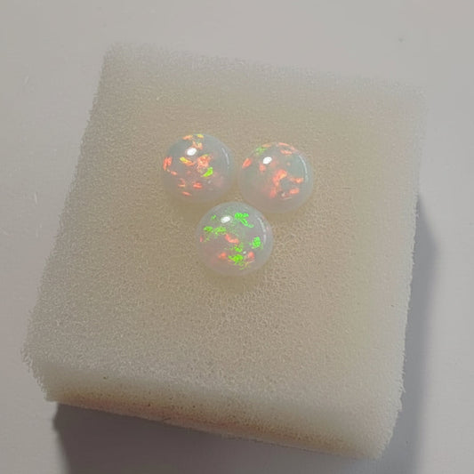Fireable White opal cabochons with red fire on a white cushion against a light background