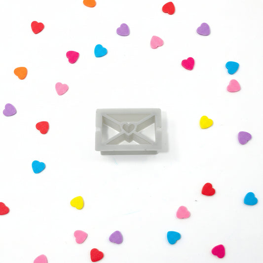 Letter-shaped cutter surrounded by colourful heart-shaped candies on a white background