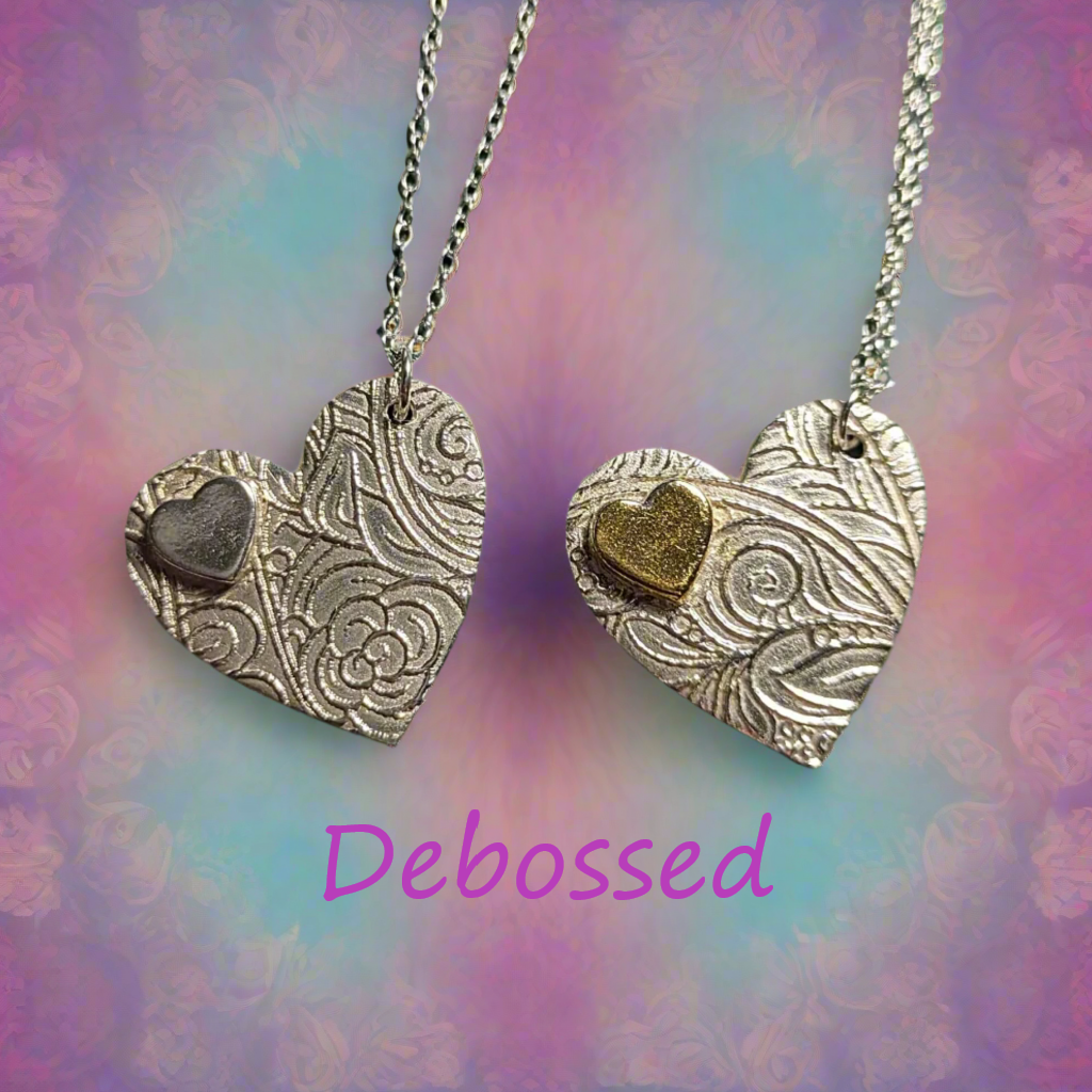 Two heart shaped pendants in 999 silver embossed with a mystic flower debossed texture mat design. One has an accent of gold.