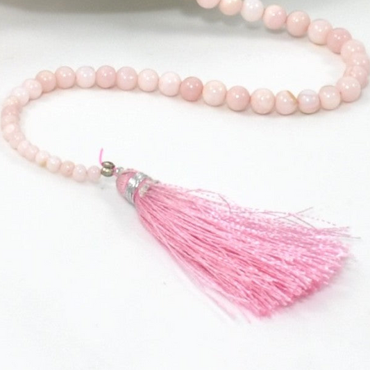 Pink beaded necklace with a tassel on a white background close up.