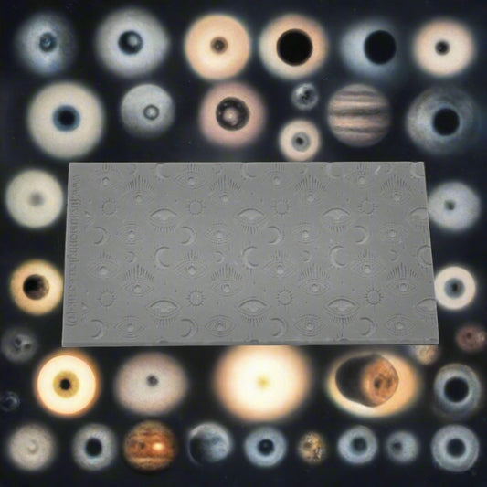 A small mystical eye repeat pattern debossed texture mat in grey material. For use on metal clay or polymer clay.