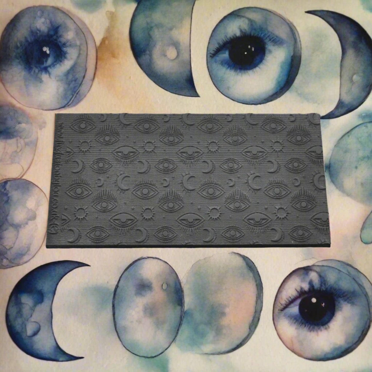A small mystical eye repeat pattern embossed texture mat in grey material. For use on metal clay or polymer clay.