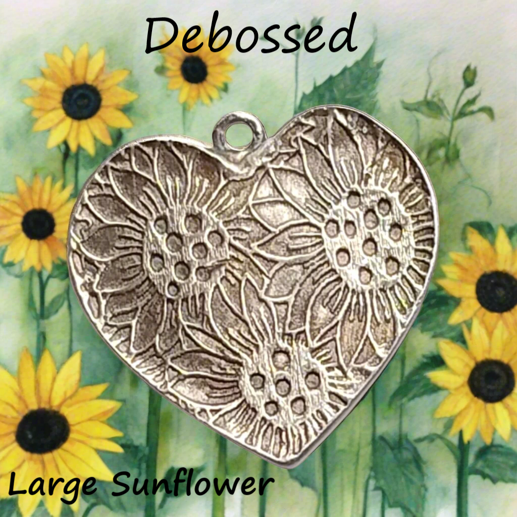 A large sunflower pattern using a debossed texture mat in silver metal clay in the shape of a heart pendant. The design shows an embossed effect on metal clay after firing.