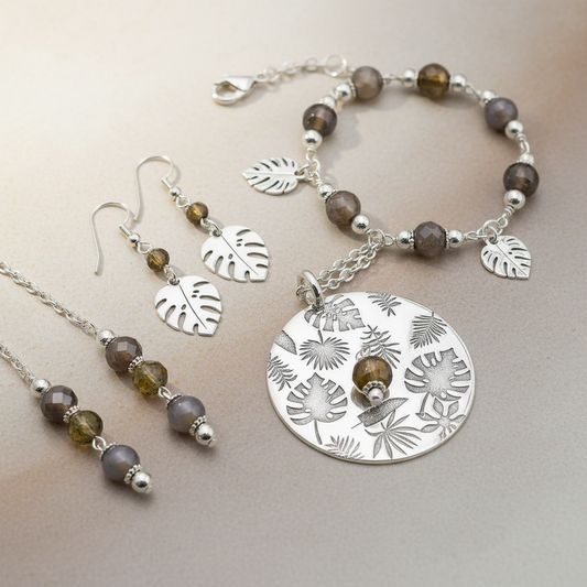 Jewellery set with silver and brown beads on a neutral background with tropical leaves pattern.