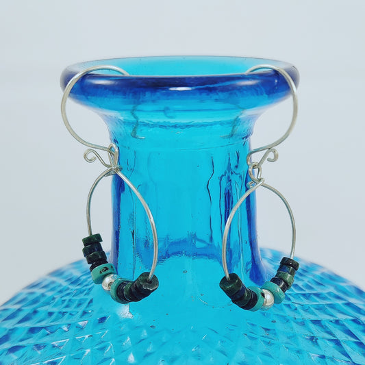 These 925 Sterling Silver hoop earrings with French hook wire feature a scroll detail. The central beads are crafted from heishi beads in shades of green, dark blue, and turquoise, along with a 925 Sterling silver ball. Light and comfortable to wear at only 2.25g each.    Length of earrings are approximately 50mm  Hoop size is 30 x 24mm  Silver ball is 5mm round and the heishi beads are graduated from 6mm x 2mm to 3mm x 2mm.  