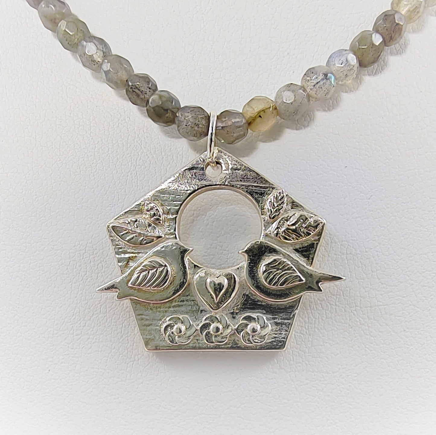 This one-of-a-kind piece is crafted with genuine Fine Silver (999) and features a birdhouse pendant depicting two love birds facing each other accented with captivating Labradorite semi-precious beads. The adjustable 925 chain and attachments provide the perfect finishing touch.