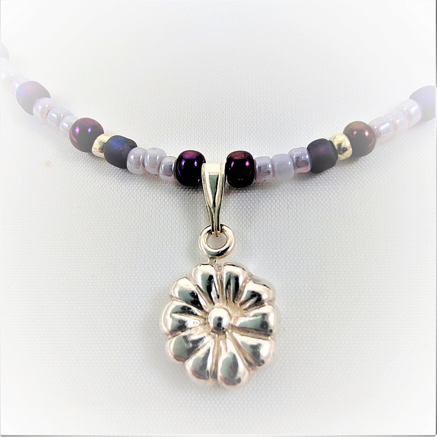 This 999 flower pendant is crafted from silver and strung on a combination of silver glass seed beads and shades of lilac purple seed beads. With a detachable pendant, you can easily switch out the pendant style or add a different type of pendant for custom styling.  