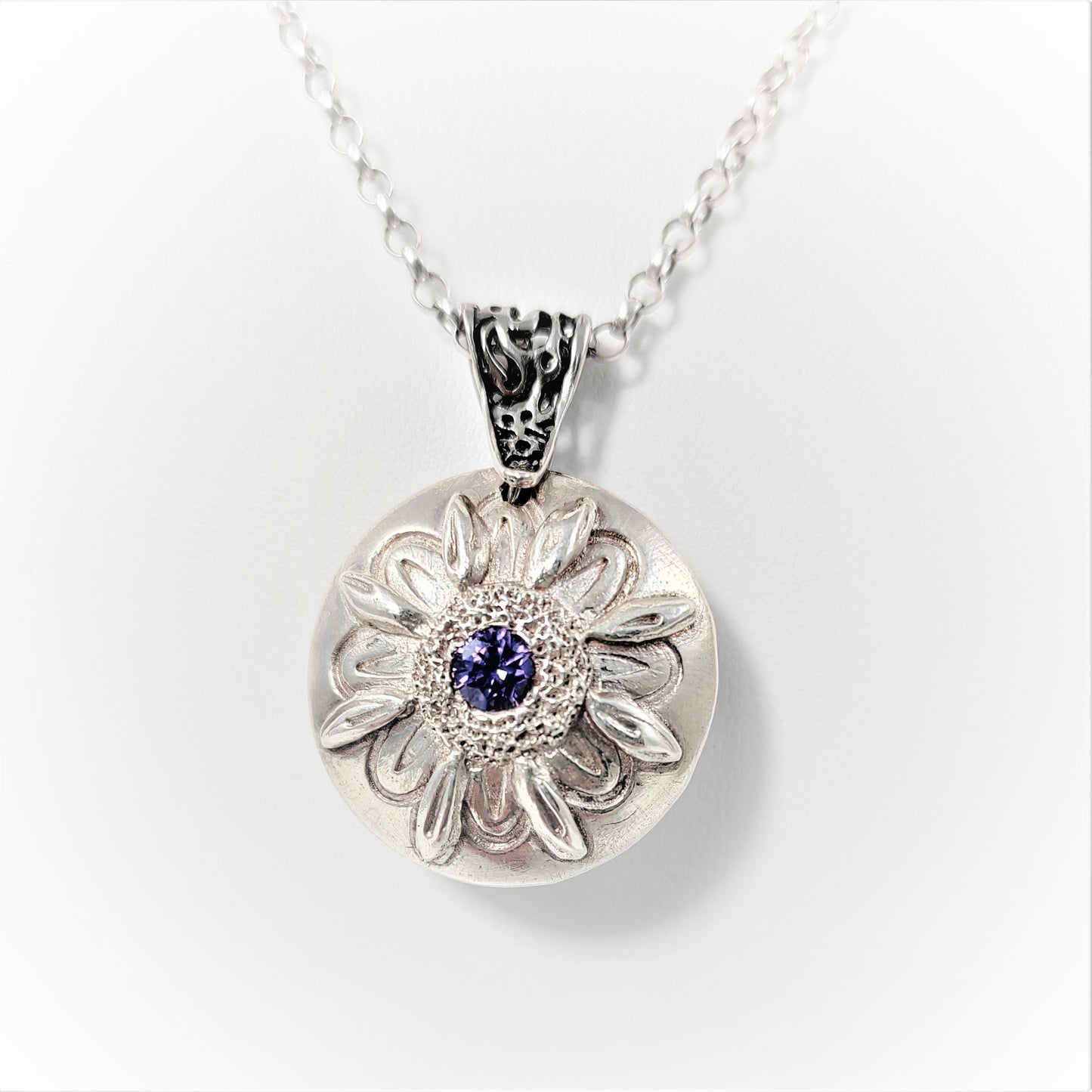 This 999 fine silver lentil bead pendant is double-sided: one features a daisy flower with a central amethyst cubic zirconia, and the other an 8-pointed flower centered on an olive cubic zirconia. It comes with a trace chain and is stamped with a London hallmark beneath the bail.  