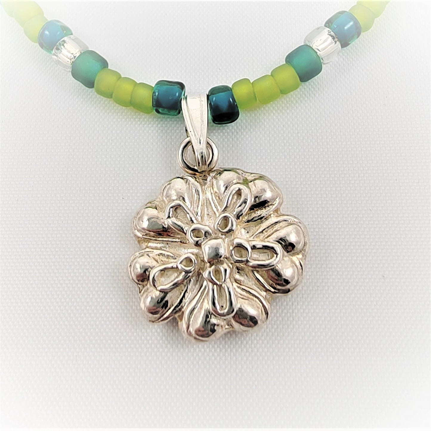 This 999 flower pendant is crafted from silver and strung on a combination of silver glass seed beads and shades of blue and green beads. With a detachable pendant, you can easily switch out the pendant style or add a different type of pendant for custom styling.  The length of the necklace including flower is approximately 19 inches  The size of flower is 17mm x 13mm  The seed bead sizes are 3mm-4mm