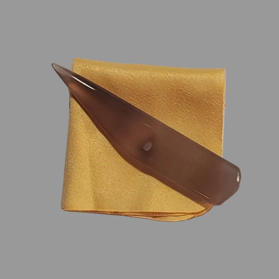 A translucent agate burnisher resting diagonally on a folded yellow microfiber cloth against a plain light grey background.
