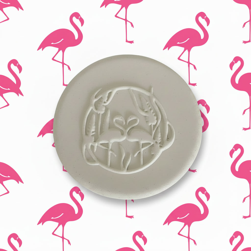 A round clay impression featuring an embossed design of two flamingos facing each other inside a circular frame with wheat stalks.