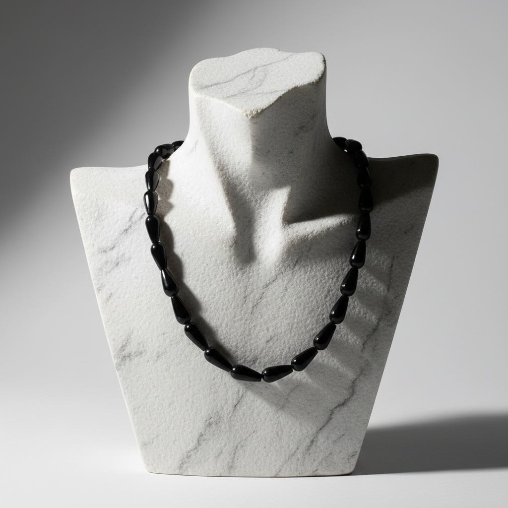Black beaded necklace on a marble bust against a gray background