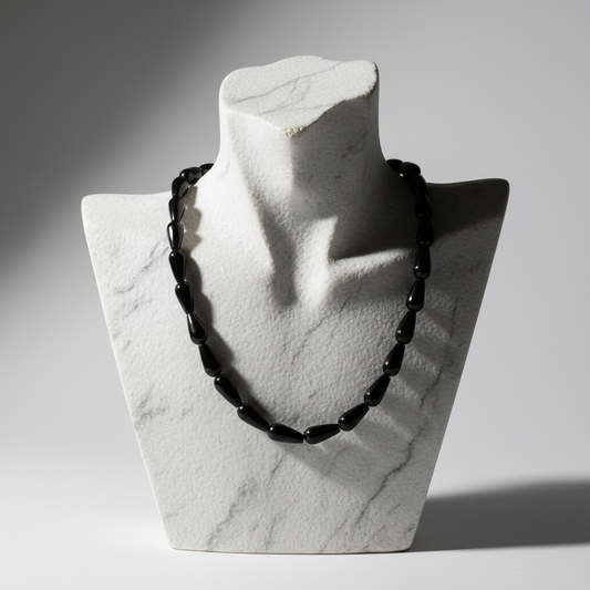 Black beaded necklace on a marble bust against a gray background