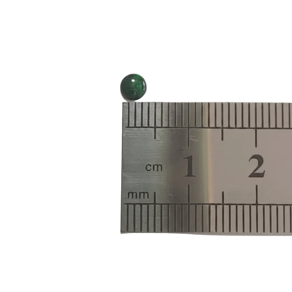 A small round green gemstone or bead shown next to a metal ruler for scale, with centimeter and millimeter markings visible on a white background.