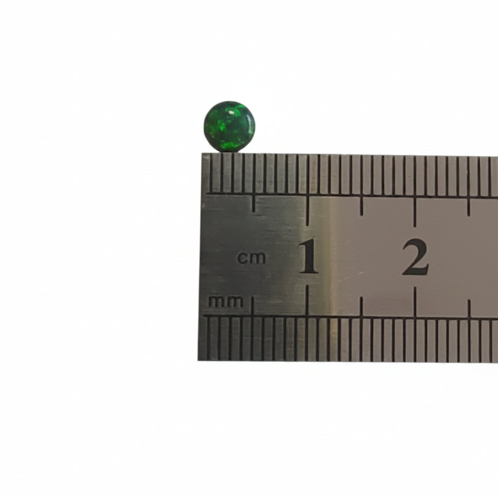 A small round green cabochon gemstone shown next to a metal ruler for scale on a plain light background.