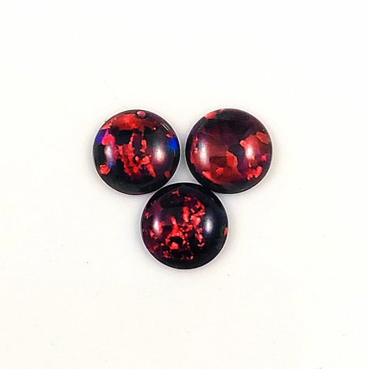 Three fireable opal red and black cabochons on a white background