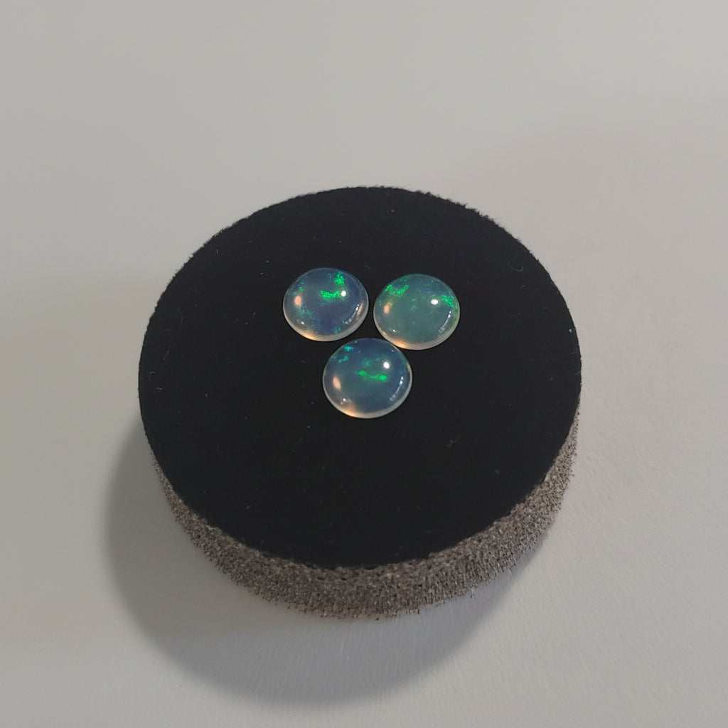 Three blue with green flash opal stones on a black cushion against a grey background