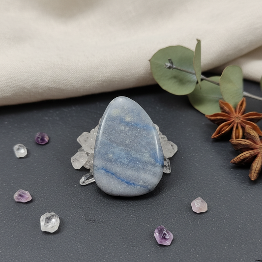 Blue stone with purple and clear crystals on a dark surface with a beige fabric background