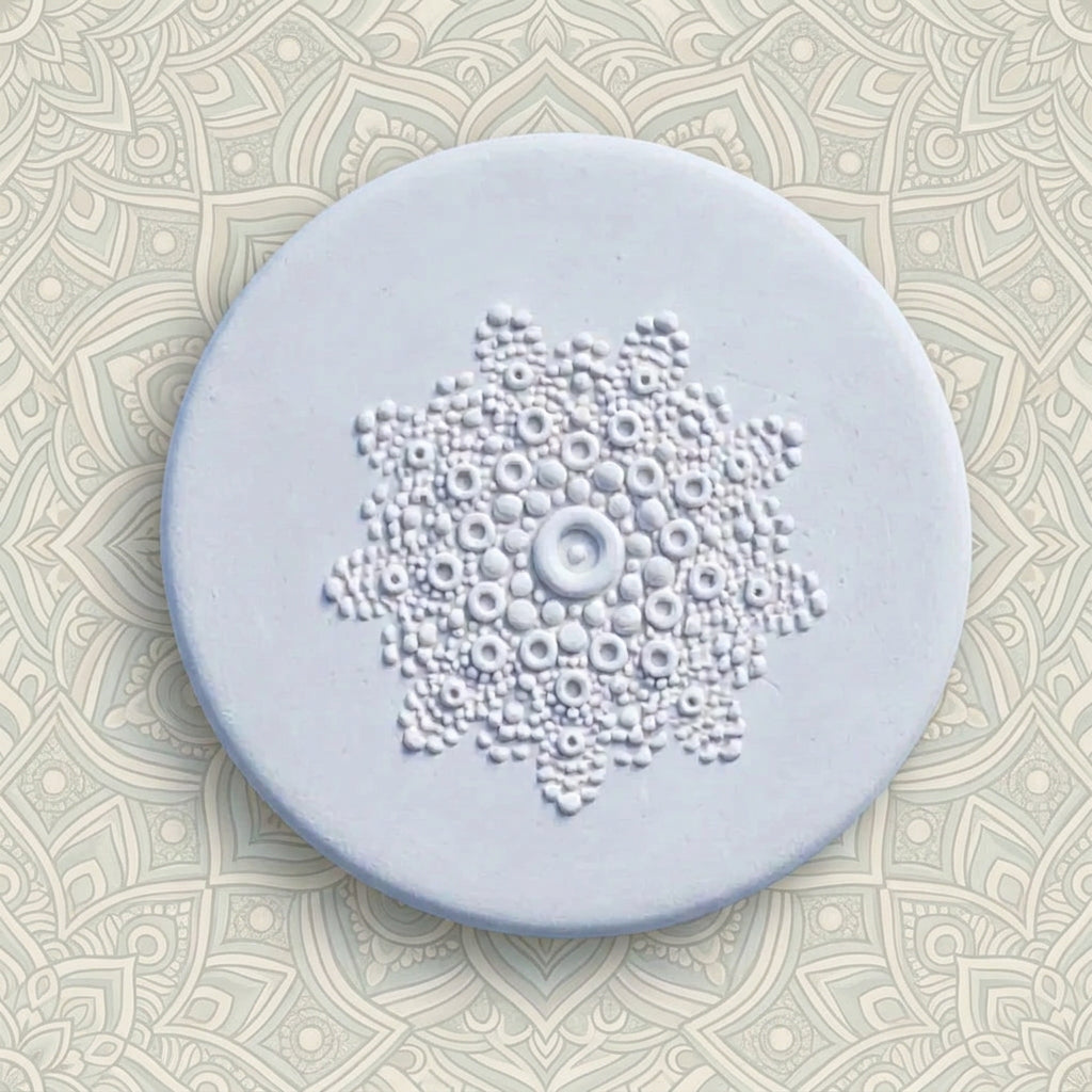 A round white clay disc with a raised circular floral or medallion pattern in the centre, photographed from above.