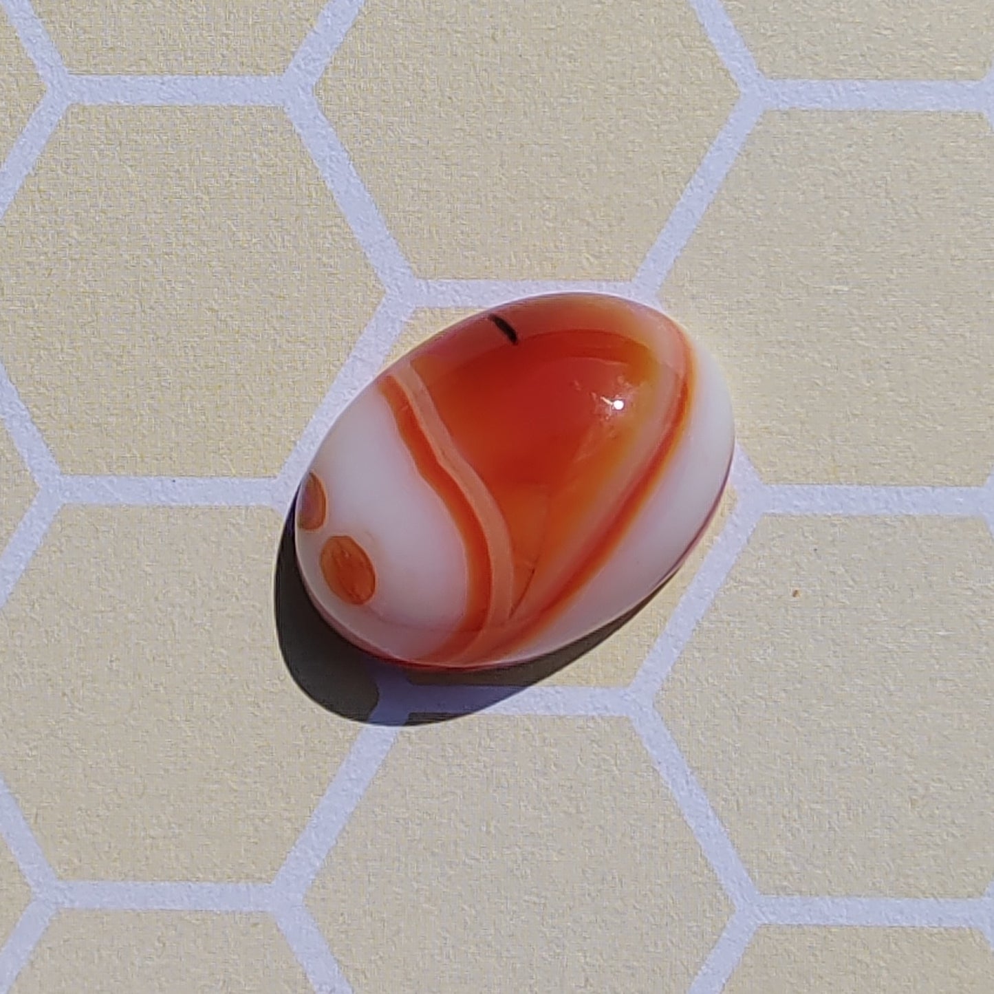 Marbled orange and white Botswana agate on a beige surface with a grid pattern