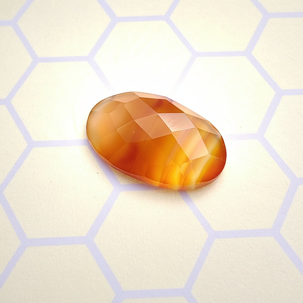 Faceted orange-brown gemstone on a light beige surface with hexagonal pattern