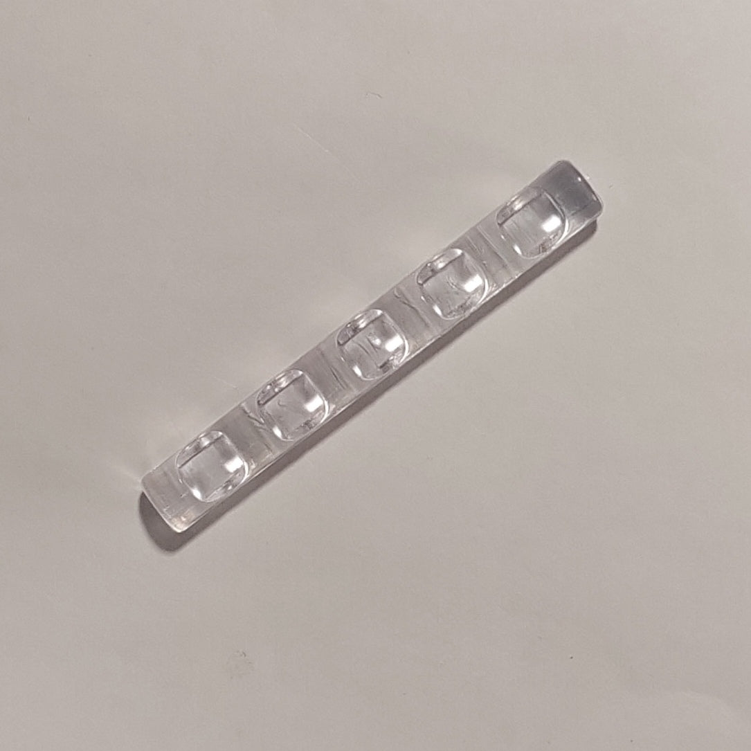 A clear plastic strip with five raised, rounded rectangular wells, photographed diagonally on a plain light gray background.
