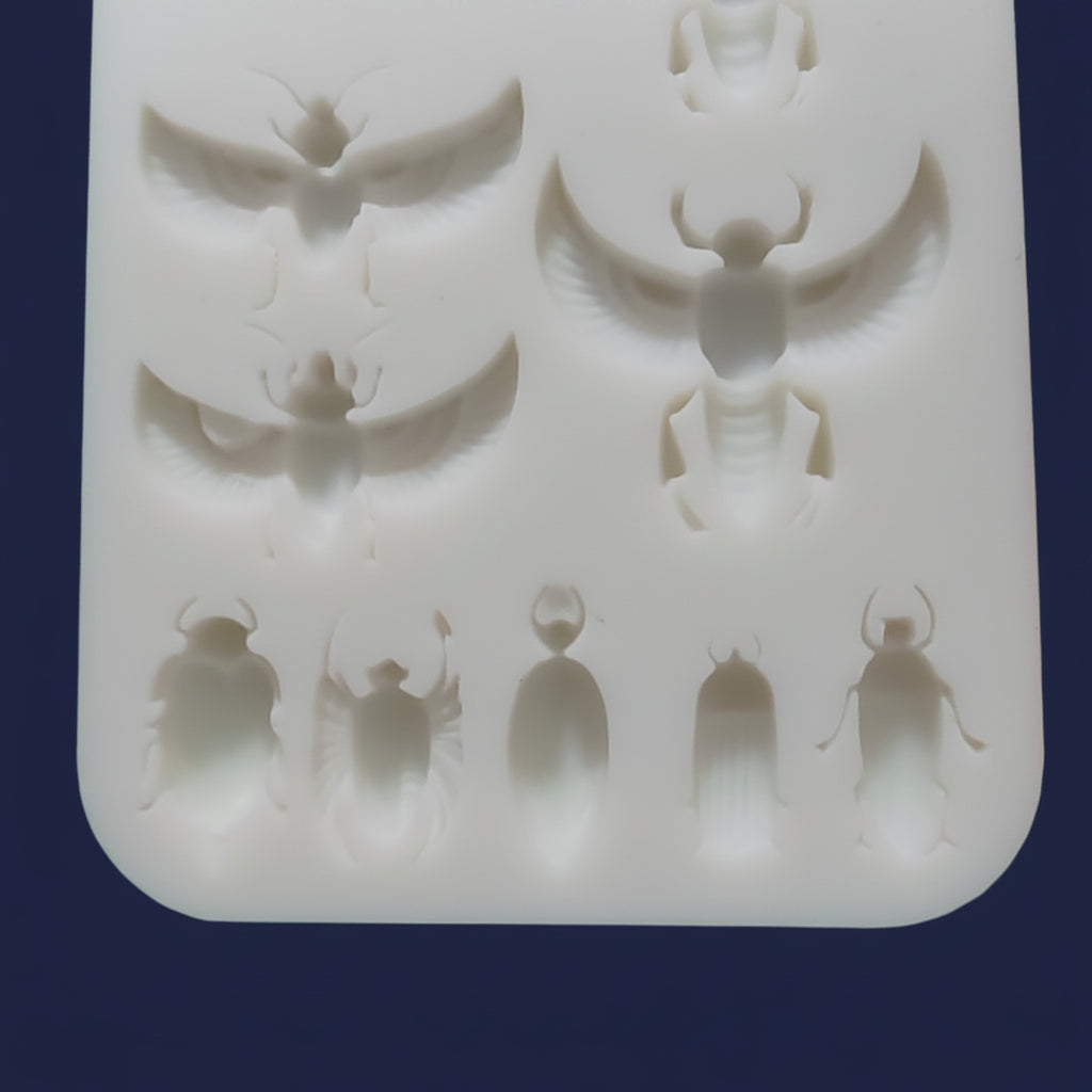 A white silicone mold tray with multiple recessed cavities shaped like beetles and small beetles.
