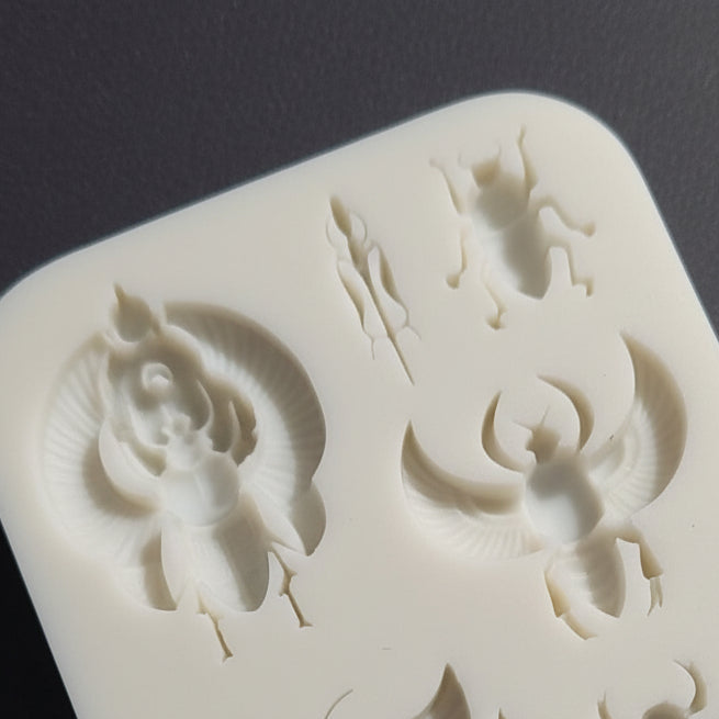 A white silicone mold tray featuring multiple insect-shaped cavities, including a large scarab beetle, and beetles