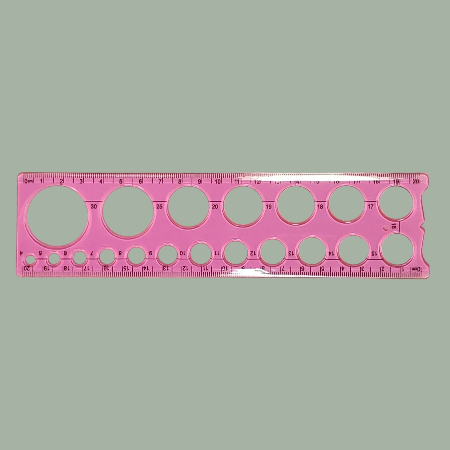 A pink plastic circular template ruler with multiple hole sizes and printed measurement markings, shown on a plain light background.