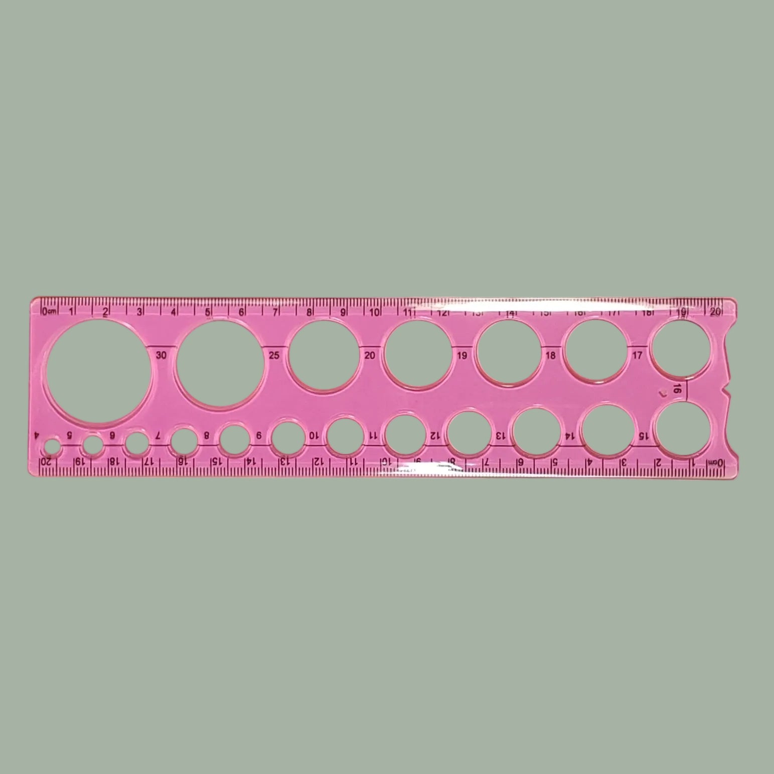 A pink plastic circular template ruler with multiple hole sizes and printed measurement markings, shown on a plain light background.