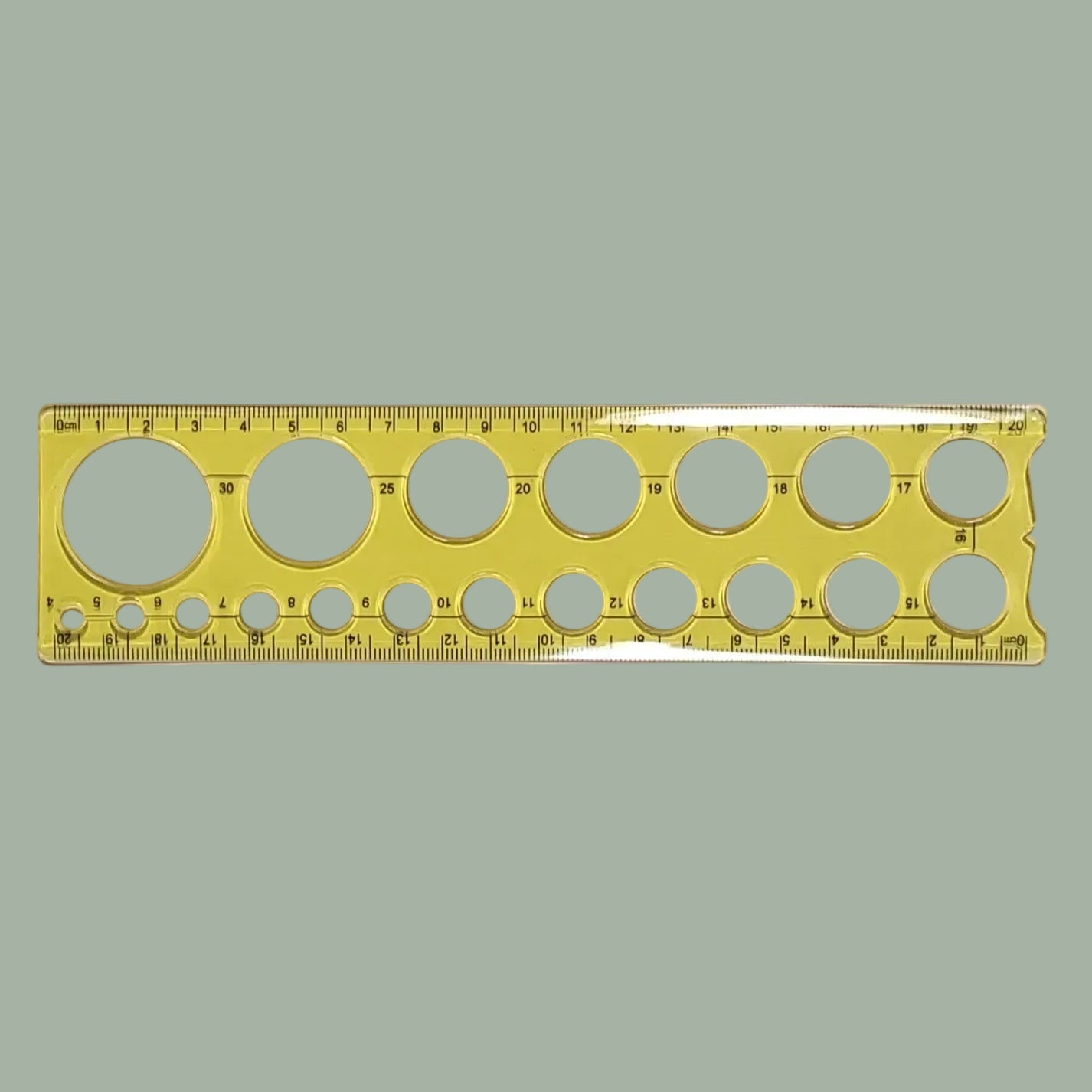 A transparent yellow plastic ruler with multiple circular cutouts of varying sizes and printed measurement markings, shown horizontally on a plain light background.