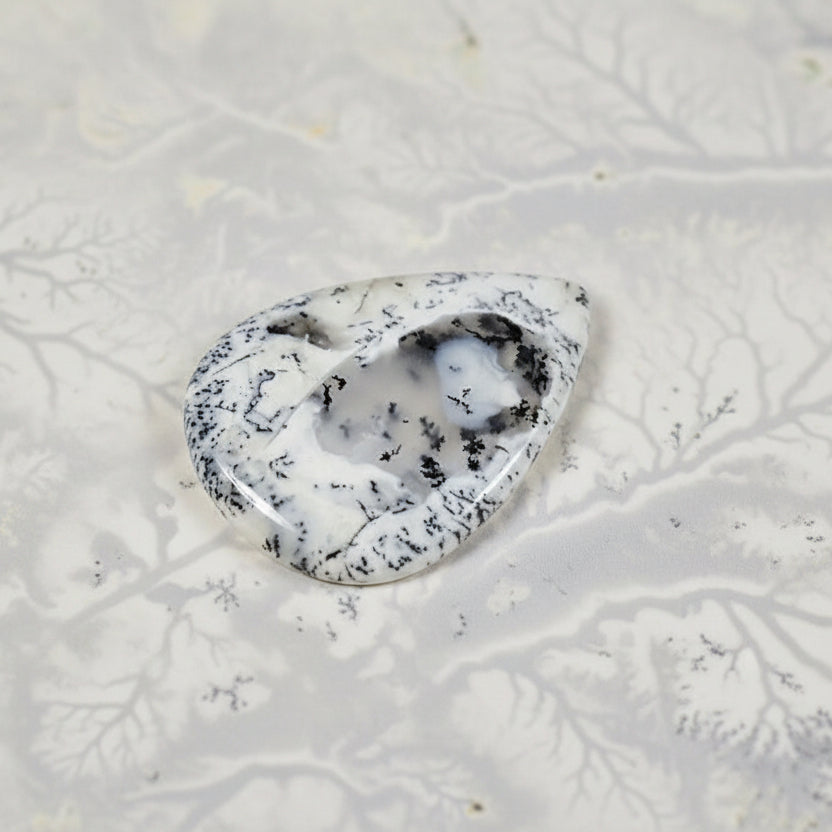 Teardrop-shaped stone with black speckles on a textured white background