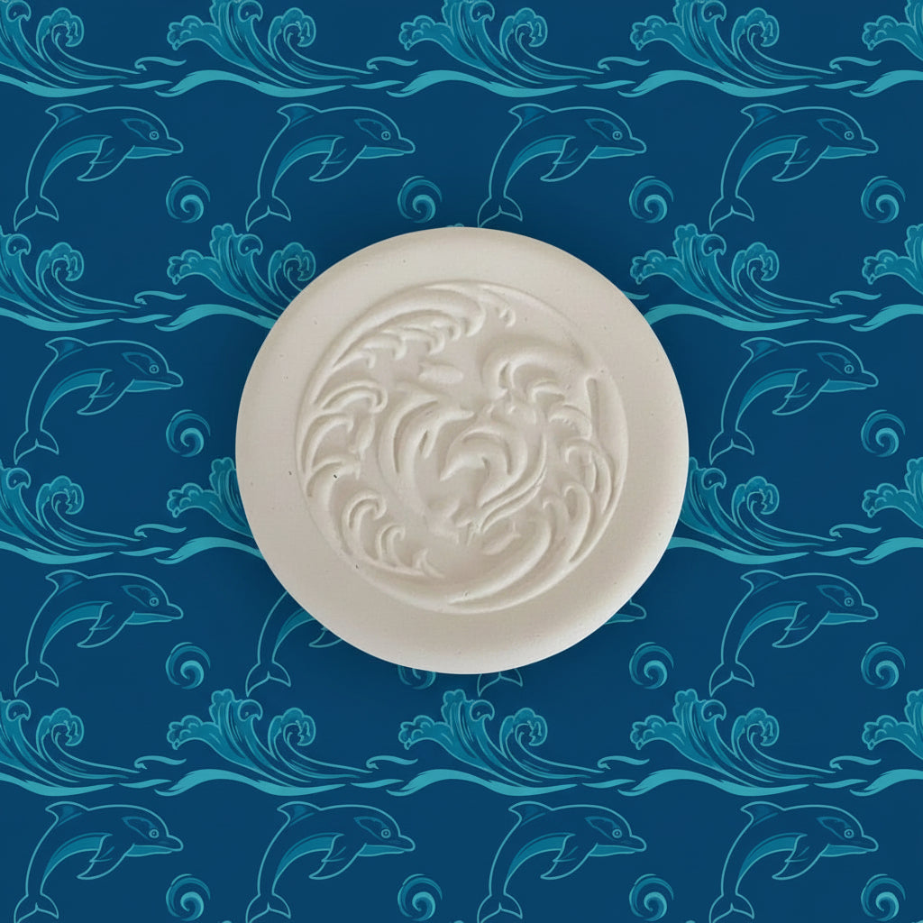 A round clay  impression with an embossed swirling dolphin pattern.