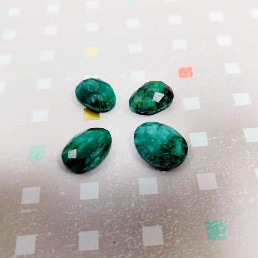 Four green emerald on a textured surface with colourful square patterns.