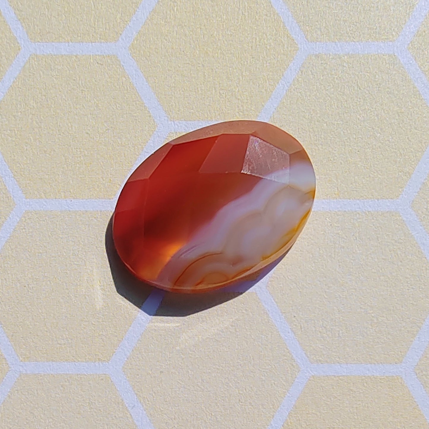 Oval-shaped red and orange stone on a beige surface with a honeycomb pattern