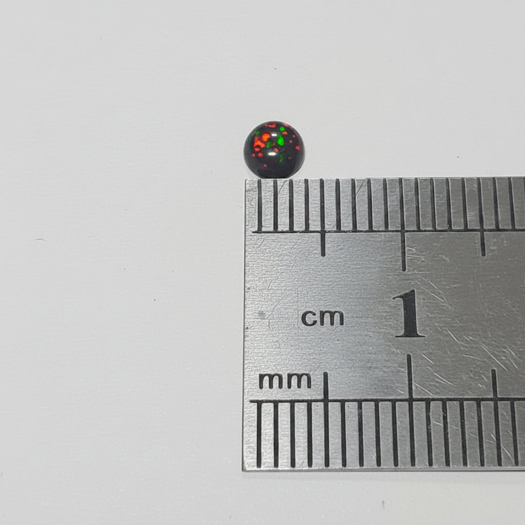 A small round black object with red and green reflective markings placed on top of a metal ruler for scale, photographed on a plain light background.