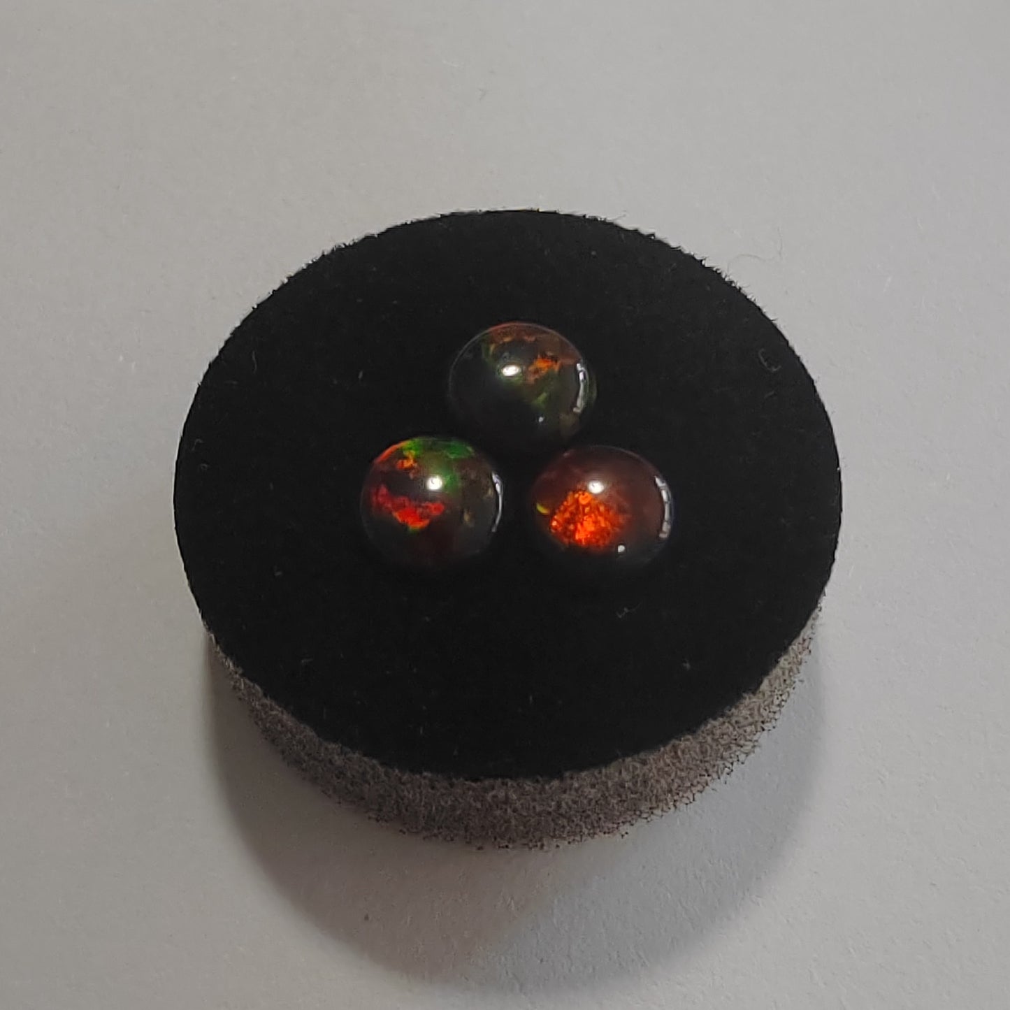 Three fire opal stones on a black cushion against a white background