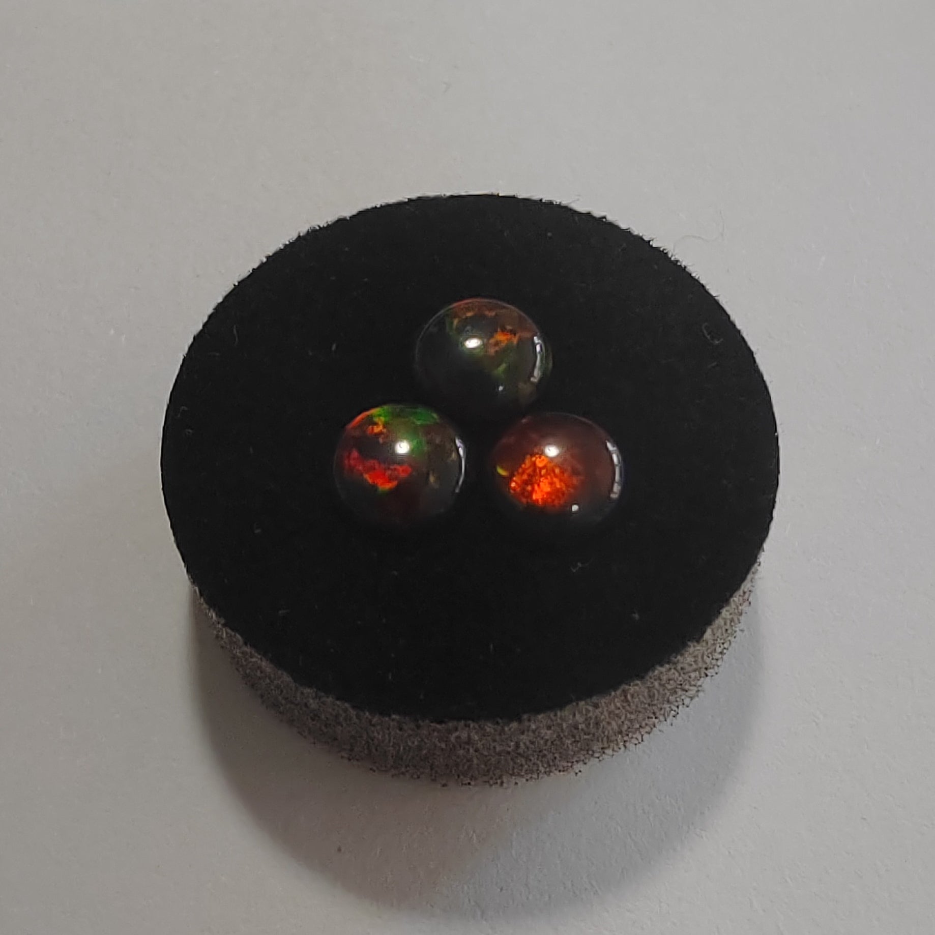 Three fire opal stones on a black cushion against a white background
