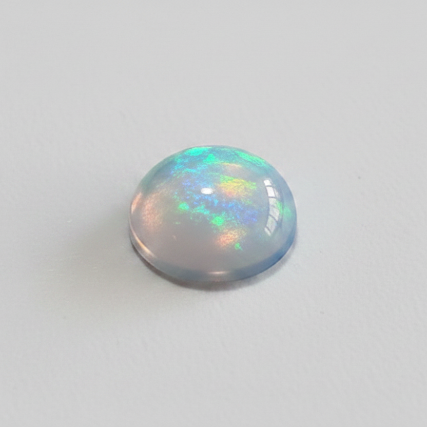 A single dome-cut cabochon gemstone with a play-of-color opal body, showing iridescent hues of green, blue, and pink on a light gray background.
