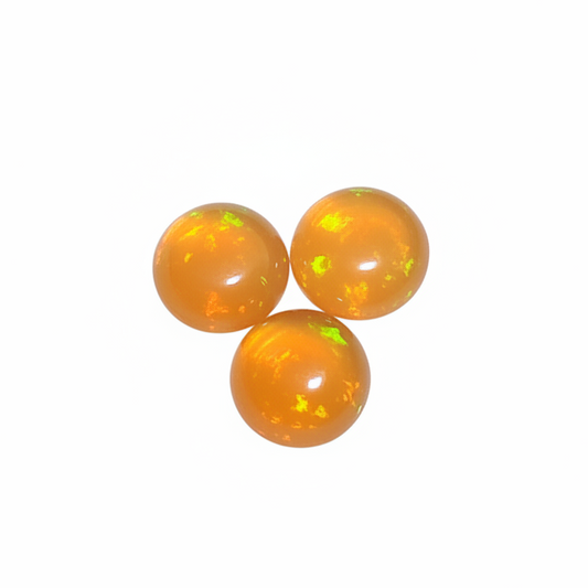 Three polished orange opal beads with vibrant yellow and green flashes, arranged in a triangle on a solid white background.