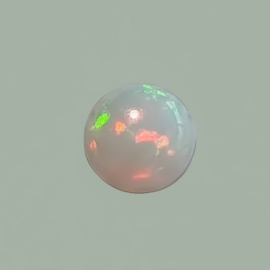 A small spherical opal gemstone with a milky white base and shifting iridescent flashes of green, pink, and orange, centered on a solid sage green background.