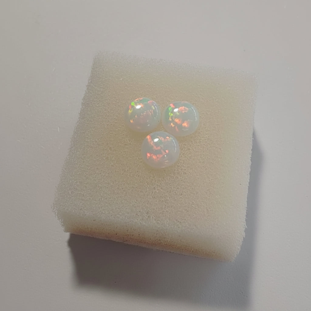 Fireable White opal cabochons with red fire on a white cushion against a light background