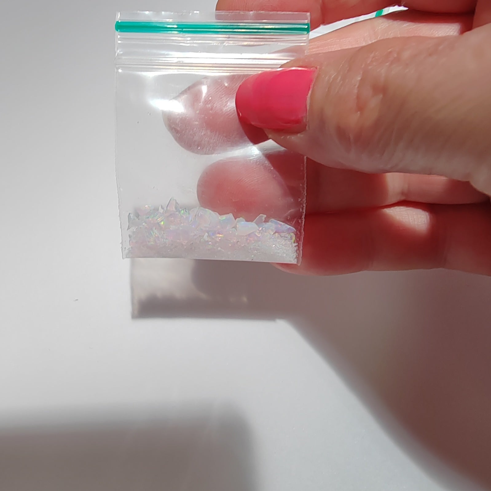 Hand holding a small clear plastic bag with fireable crushed pink opal with green flash against a white background
