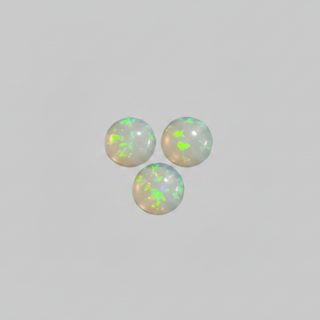 Three round white opal cabochons with vibrant green and blue flashes, arranged in a triangle on a solid gray background.