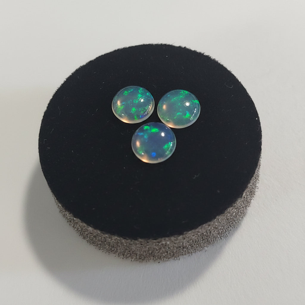 Three water opal cabochons on a black cushion against a grey background
