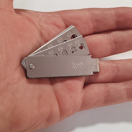 A metallic multi-size gem measuring set arranged in a circular fan shape in the palm of a hand.