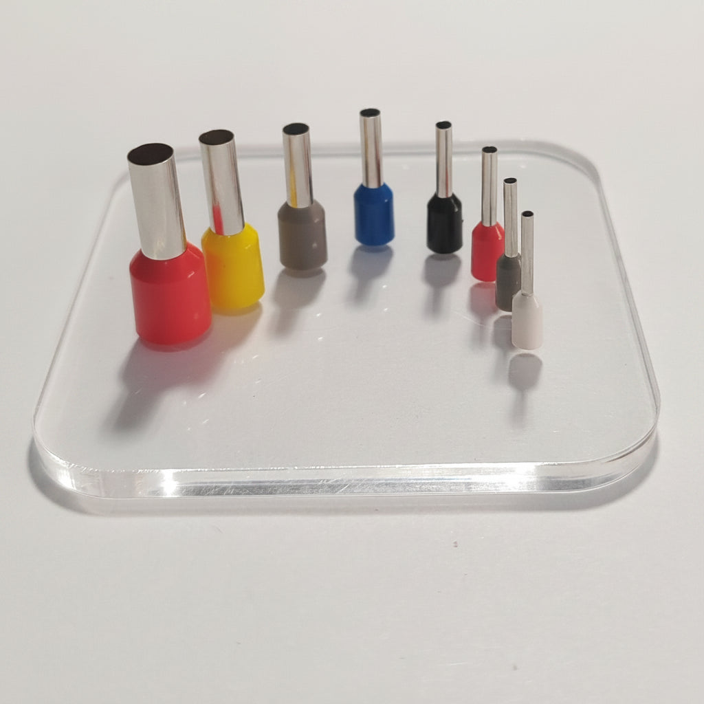 A set of small cylindrical hole punches arranged on a clear acrylic stand against a plain light background. The bits have silver metal shanks and colourful bodies in red, yellow, grey, blue, black, pink, and white.